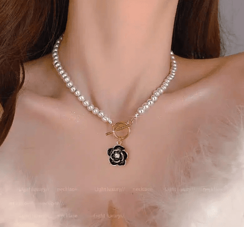 Woman wearing pearl necklace with gold clasp and black flower pendant