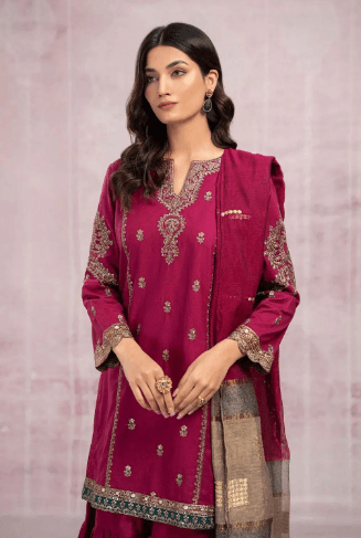 Woman wearing a maroon embroidered traditional outfit with gold detailing, set against a light background.