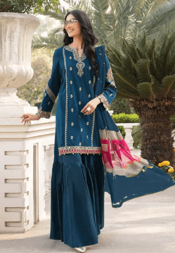 Woman in a blue embroidered ethnic suit with dupatta posing outdoors by palm trees