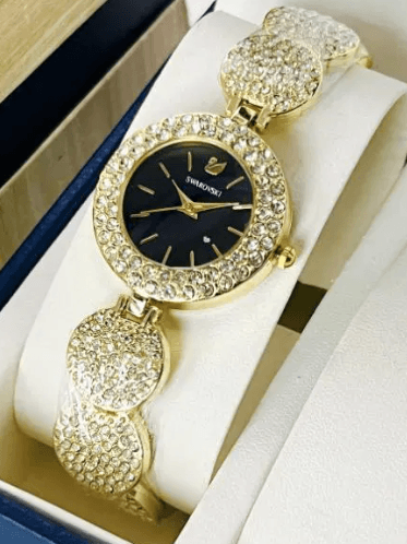 Gold women’s watch with black dial and crystal-studded band on display pillow