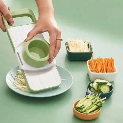 Hand using vegetable slicer to cut julienne strips, with sliced cucumbers, carrots, potatoes in bowls.
