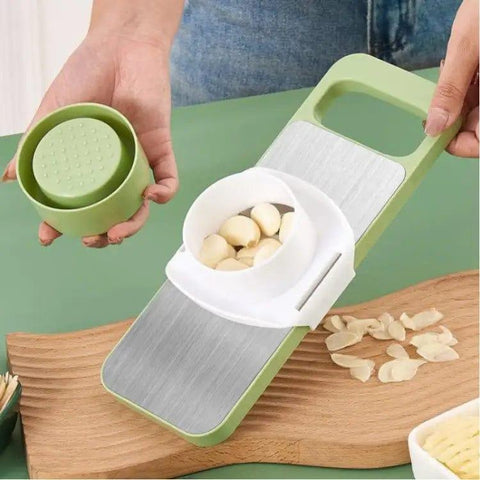Hand using green and white garlic slicer kitchen tool with fresh garlic cloves on cutting board