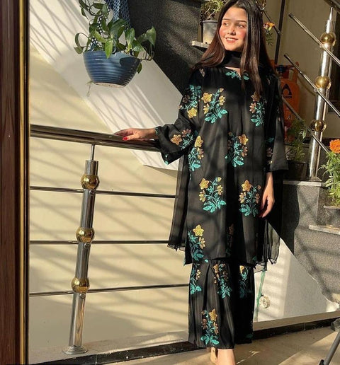 Woman in black floral embroidered kurta set standing indoors near stairs and plants